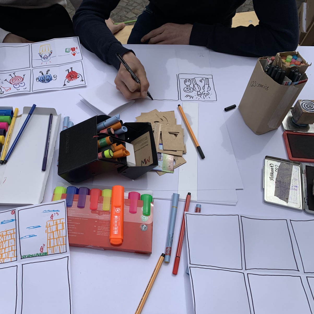 Eine Person zeichnet an einem Tisch mit Zeichenutensilien und Comicstrips.